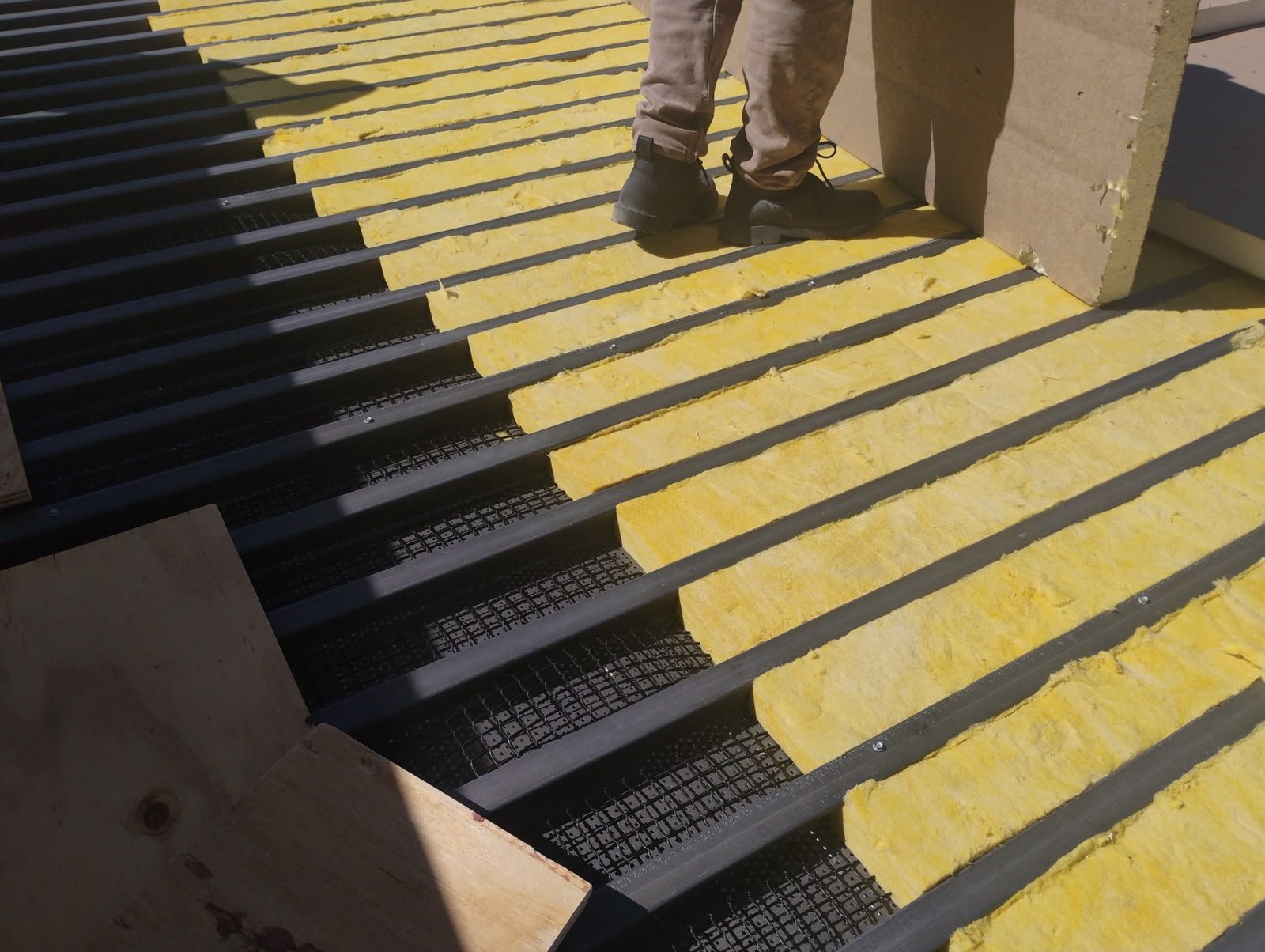 Roofer installing insulation batts between metal deck channels